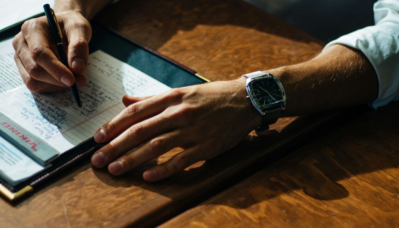 person writing on paper leaning on brown table