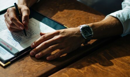 person writing on paper leaning on brown table
